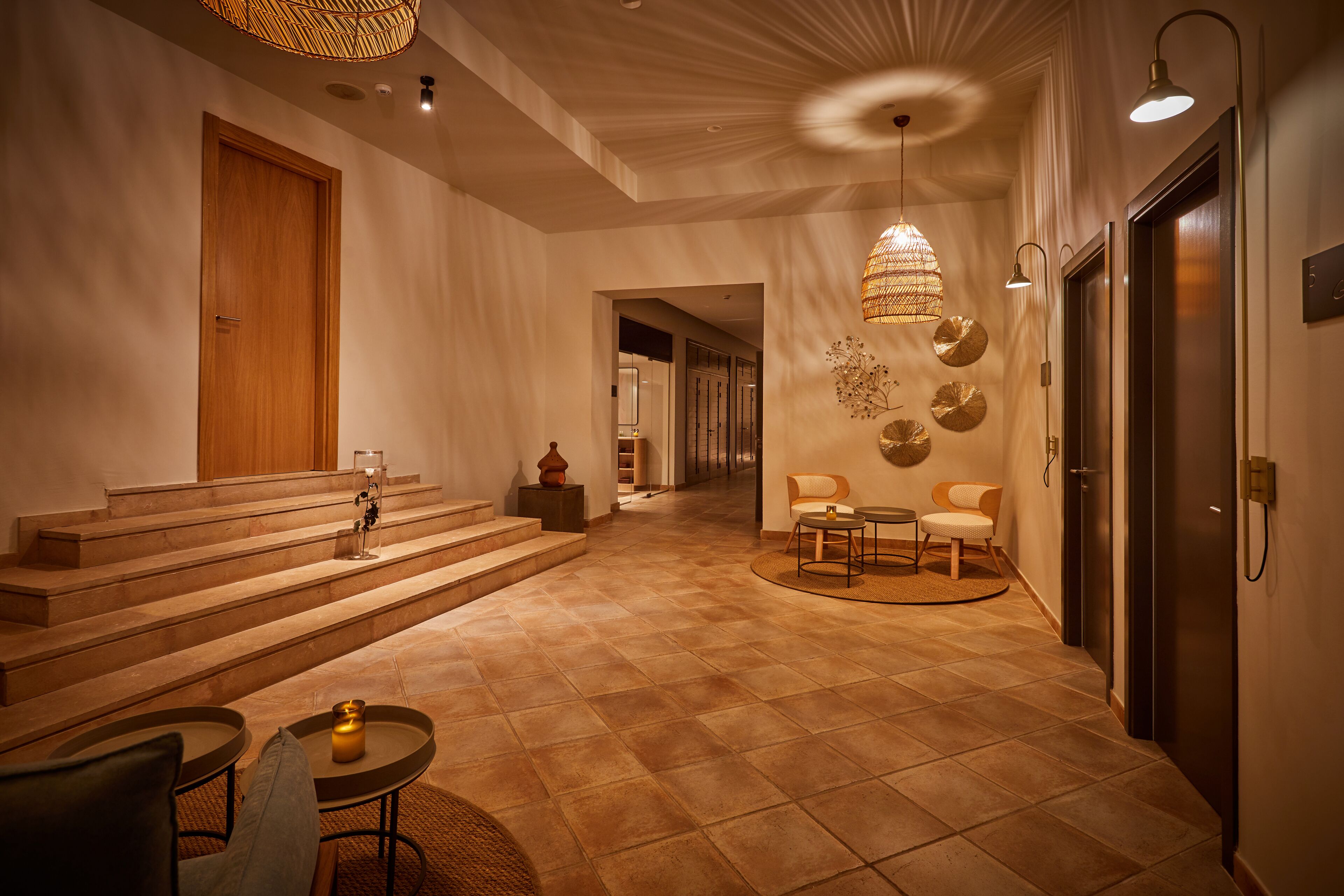 Un interior moderno con una escalera que conduce a un nivel superior, una zona de estar con una mesa redonda y una pared decorativa con motivos circulares.