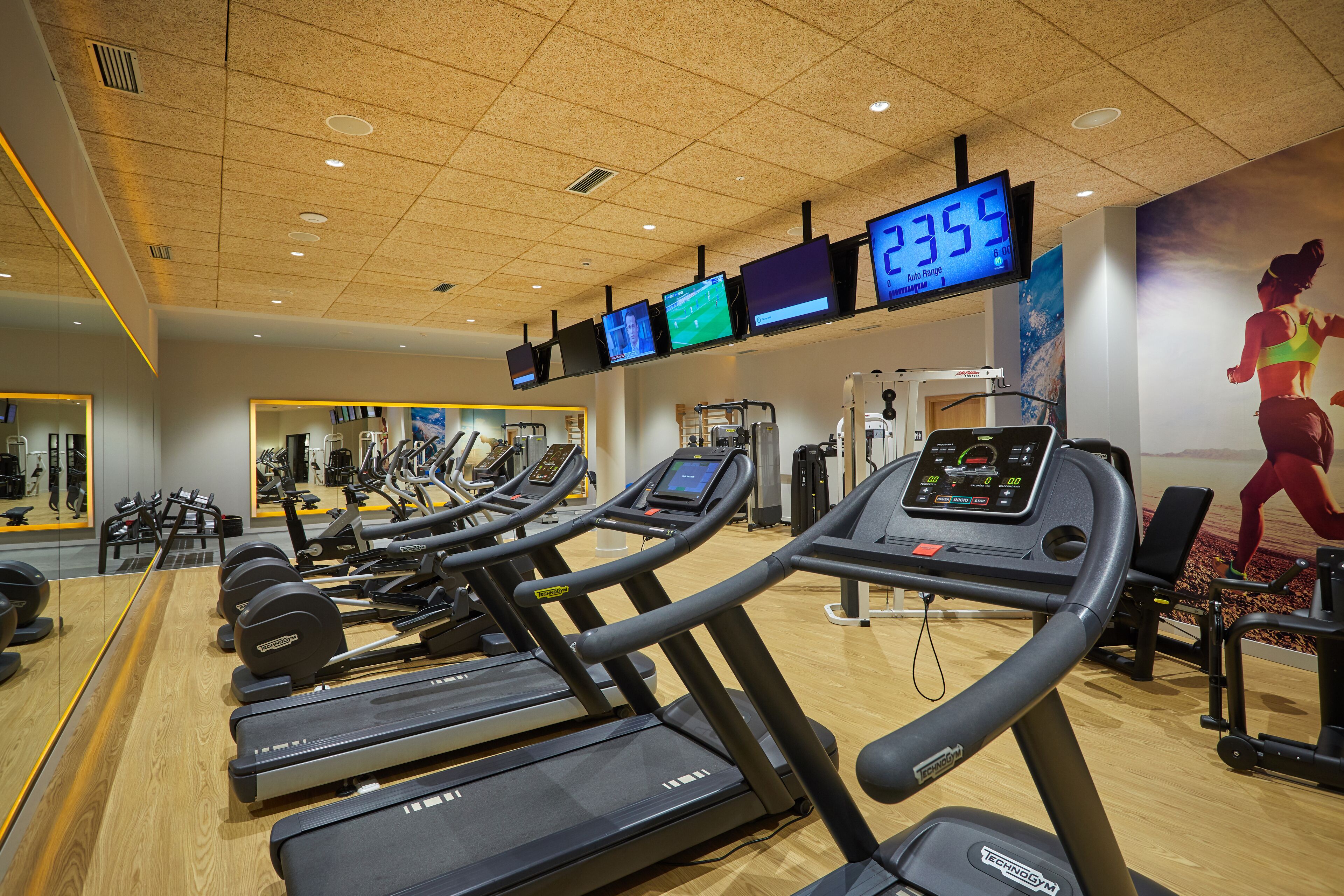 A gym with treadmills, weight machines, and a digital display showing workout metrics.