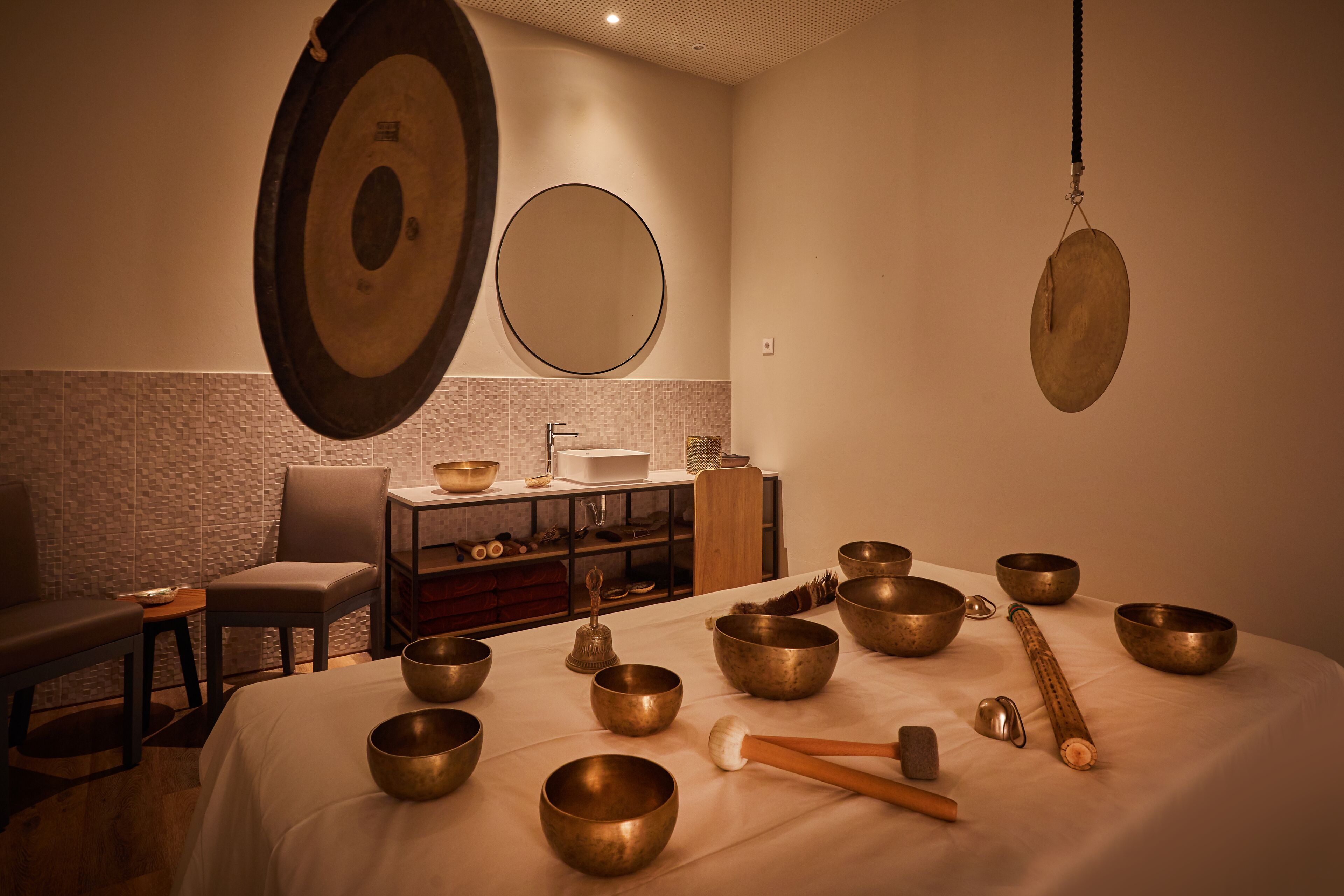 A room with a bed, several meditation bowls, a wooden mallet, and a hanging gong.