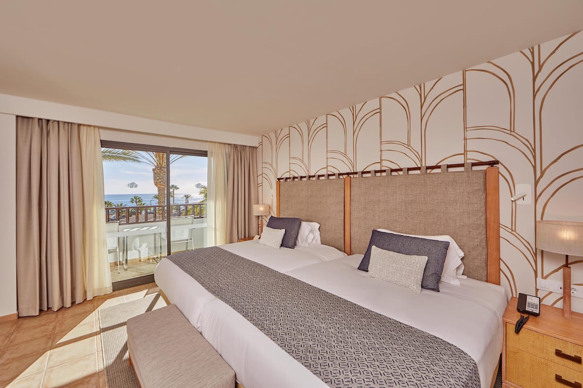 A hotel room with a large bed, a balcony with a view of the beach, and a modern design.