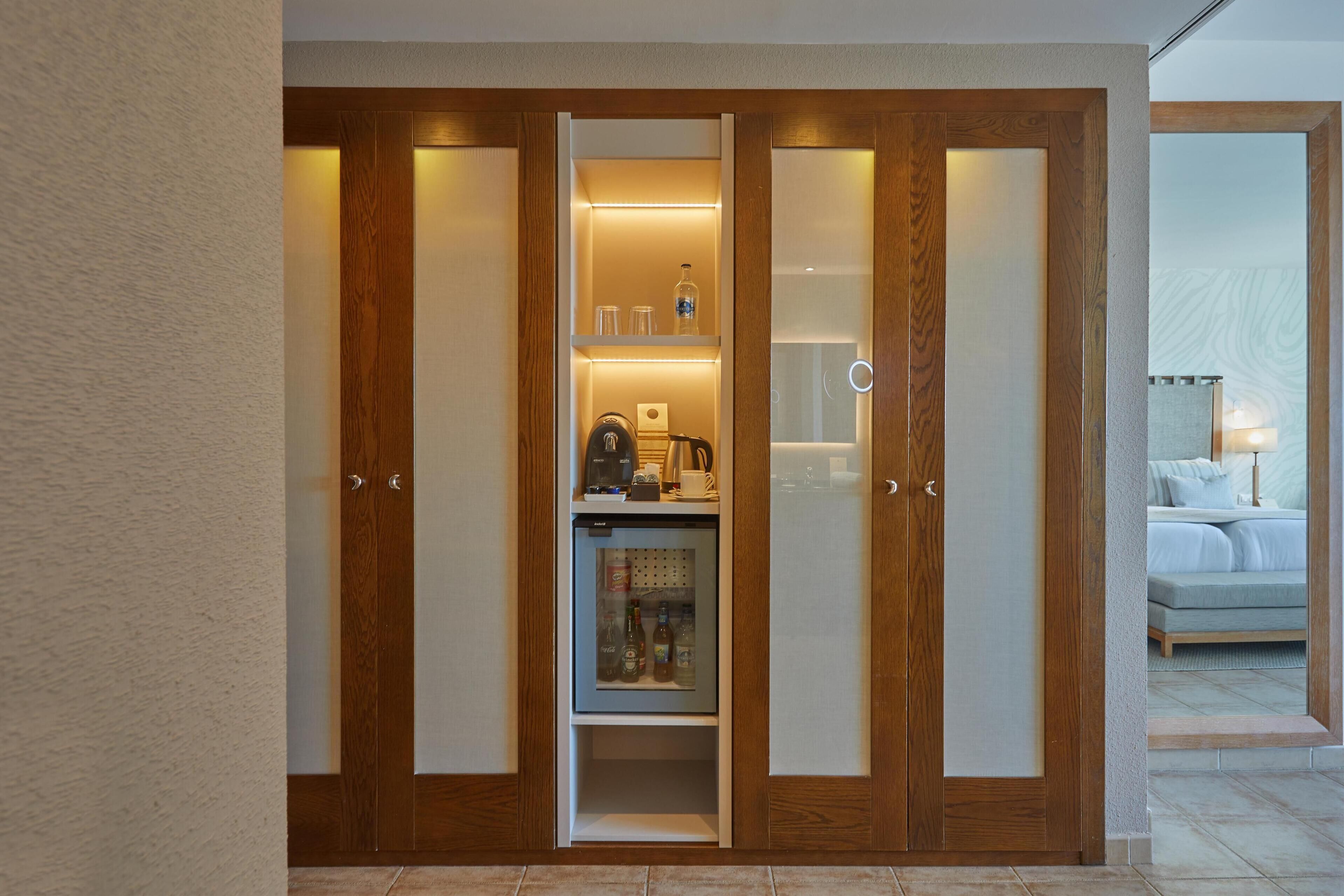 Una camera d'albergo con un armadio in legno, un minibar con macchina del caffè e un letto con comodino.