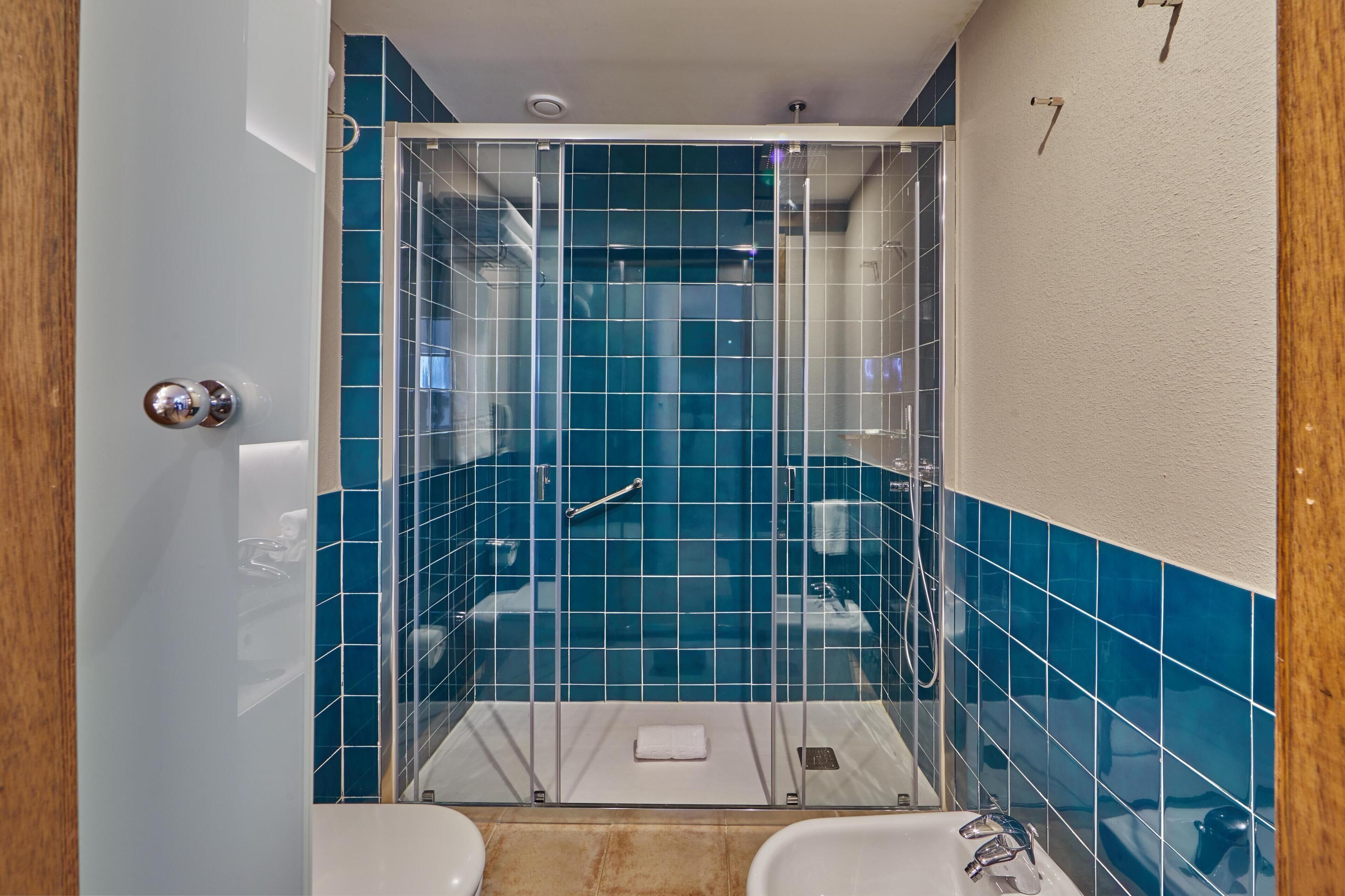 A small bathroom with a glass-enclosed shower, white and blue tiles, and a white towel on the floor.