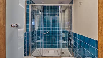 A small bathroom with a glass-enclosed shower, white and blue tiles, and a white towel on the floor.