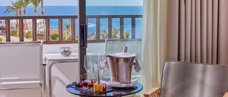 A balcony with a table set for two, a chair, and a view of the sea.