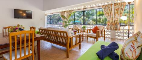 A room with a dining table, wooden chairs, a sofa, and a green mat.