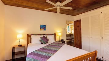 A hotel room with a bed, two bedside lamps, a ceiling fan, a painting on the wall, and a wooden door.