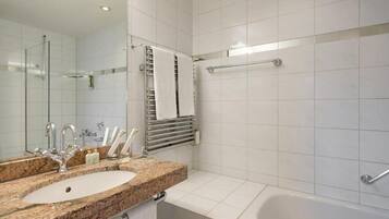 Une salle de bain moderne avec un lavabo surmonté d’un plan de travail en granit, un grand miroir, une douche à parois de verre et une baignoire blanche.