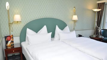 Habitación de hotel con una cama grande, dos lámparas de noche, una mesita de noche con un libro y un cabecero verde.