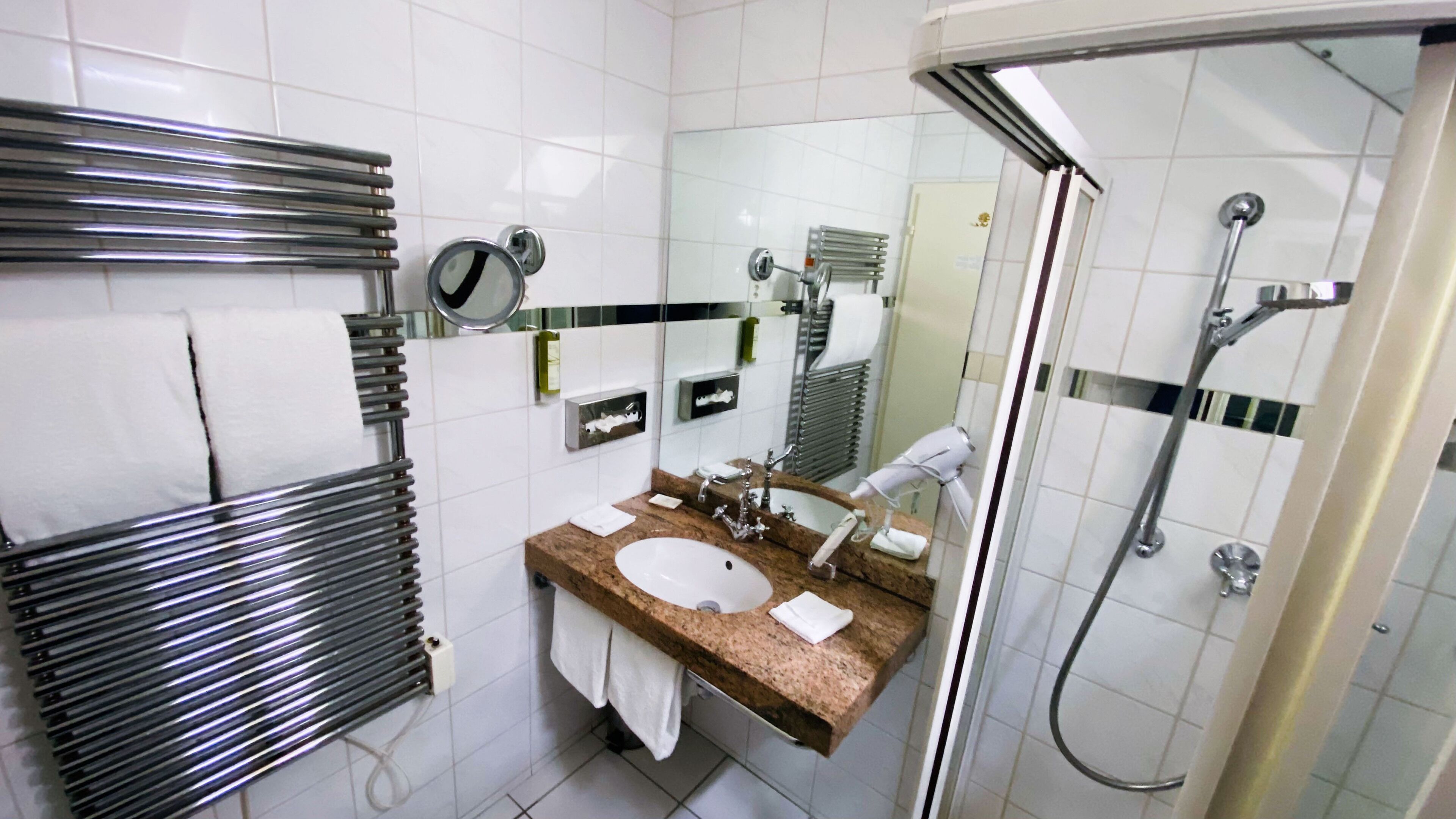 A modern bathroom with a glass-enclosed shower, a sink with a marble countertop, and a towel rack with white towels.