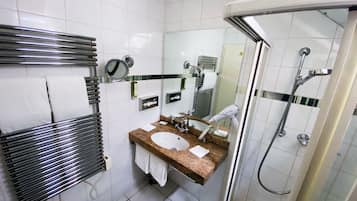 A modern bathroom with a glass-enclosed shower, a sink with a marble countertop, and a towel rack with white towels.