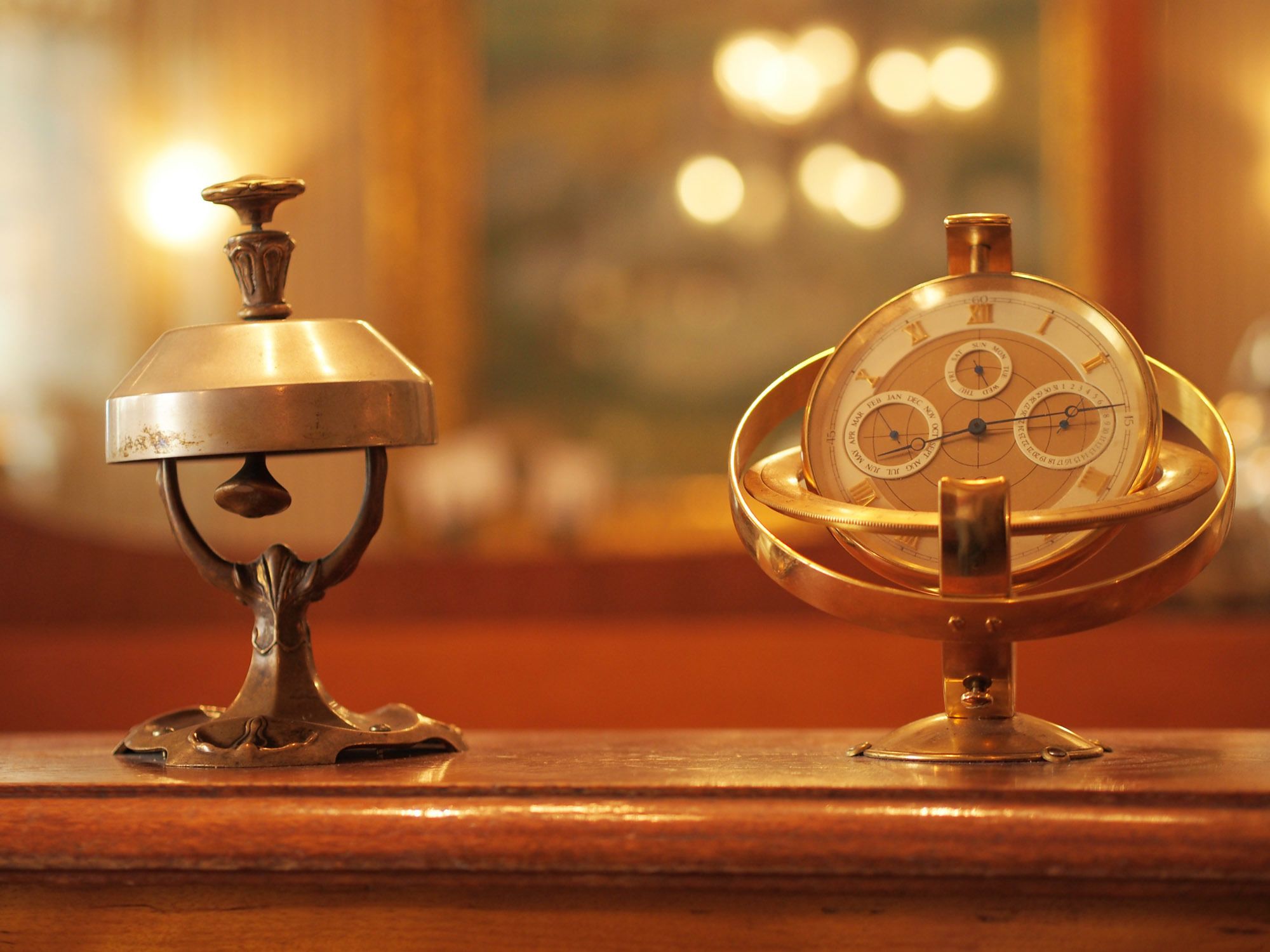 A brass astronomical clock and a brass lamp on a wooden surface.