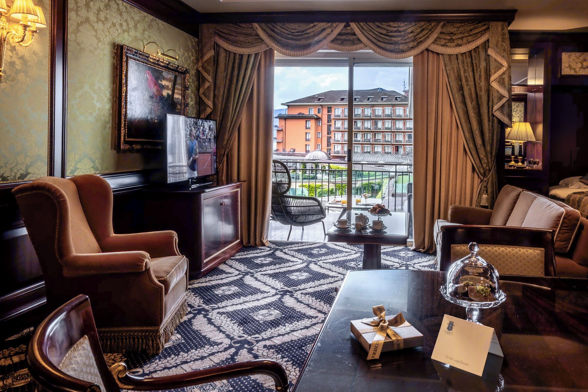Habitación de hotel con un ventanal grande, televisión, sofá, mesa de centro y comedor con vistas a la ciudad.