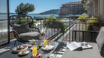 A balcony with wicker furniture, a table set with breakfast items, and a view of a lake and buildings.