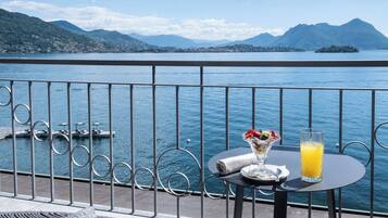 Un balcón con una mesa dispuesta para una comida, con vista a un lago y montañas al fondo.