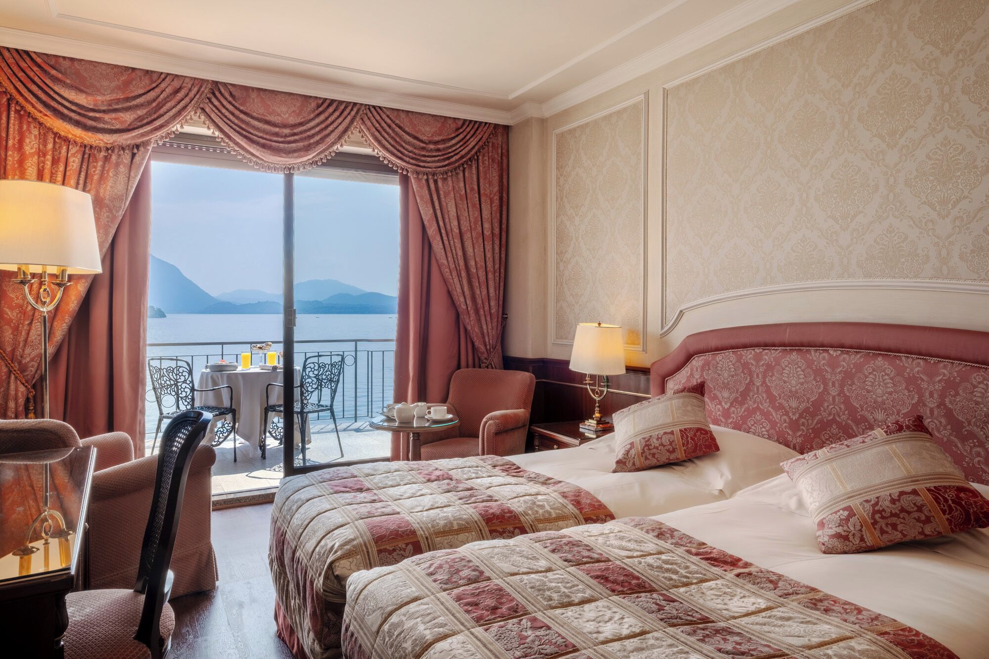 Quarto de hotel com uma cama grande, duas cadeiras, uma mesinha e varanda com vista para o mar.
