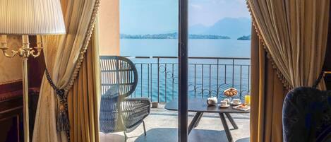 A room with a view of the sea, featuring a blue patterned carpet, a sofa, a chair, and a table with breakfast items.