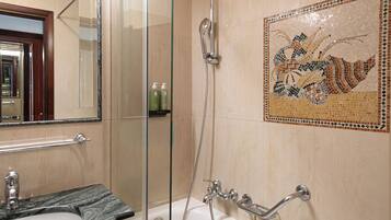 Un baño con cabina de ducha de vidrio, bañera con barra de apoyo, lavamanos con encimera de mármol y pared de mosaicos.