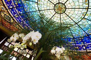 Un plafond en vitrail orné de motifs complexes et décoré d’orchidées blanches.