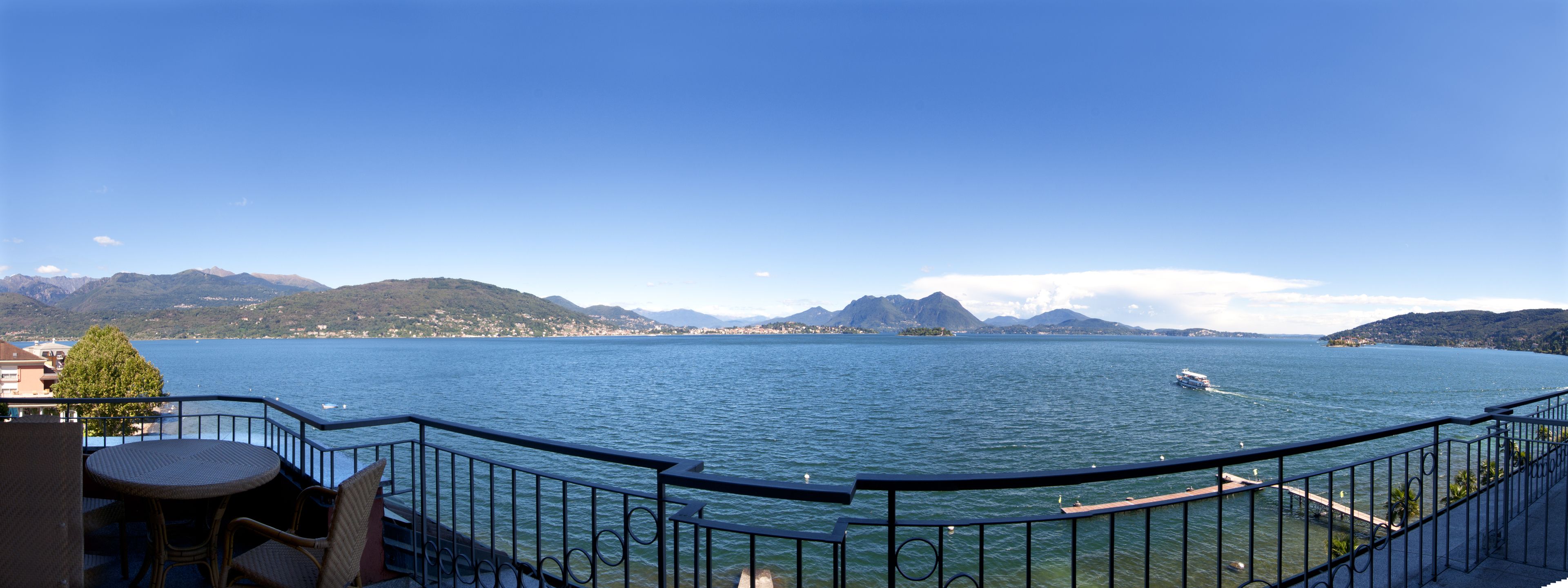 A balcony with wicker furniture overlooking a lake with mountains in the background.