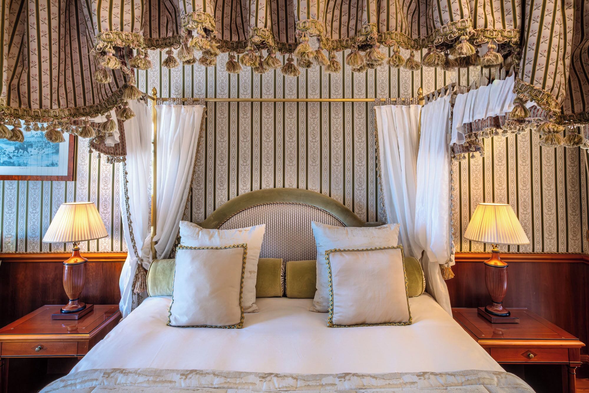 A four-poster bed with white linens and decorative pillows, flanked by two bedside tables with lamps.