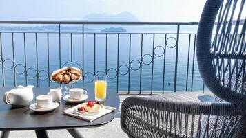 Un balcón con una mesa dispuesta para el desayuno, una silla de mimbre y vista al mar.