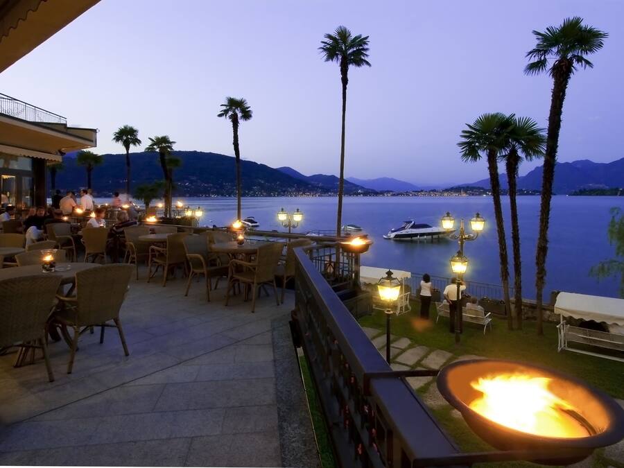 An outdoor dining area with tables and chairs, a fire pit, and a view of the water and mountains.