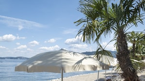 A beach with sun loungers and umbrellas, palm trees, and a clear view of the sea. - Grand Hotel Dino (Baveno)