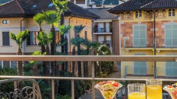 A terrace with a table set for two, featuring a drink and a fruit dish. The terrace overlooks a mountainous landscape with traditional buildings.