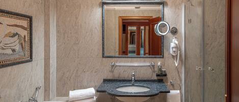 A bathroom with a marble wall, a sink, a bathtub, a glass shower enclosure, a mirror, and a towel rack.