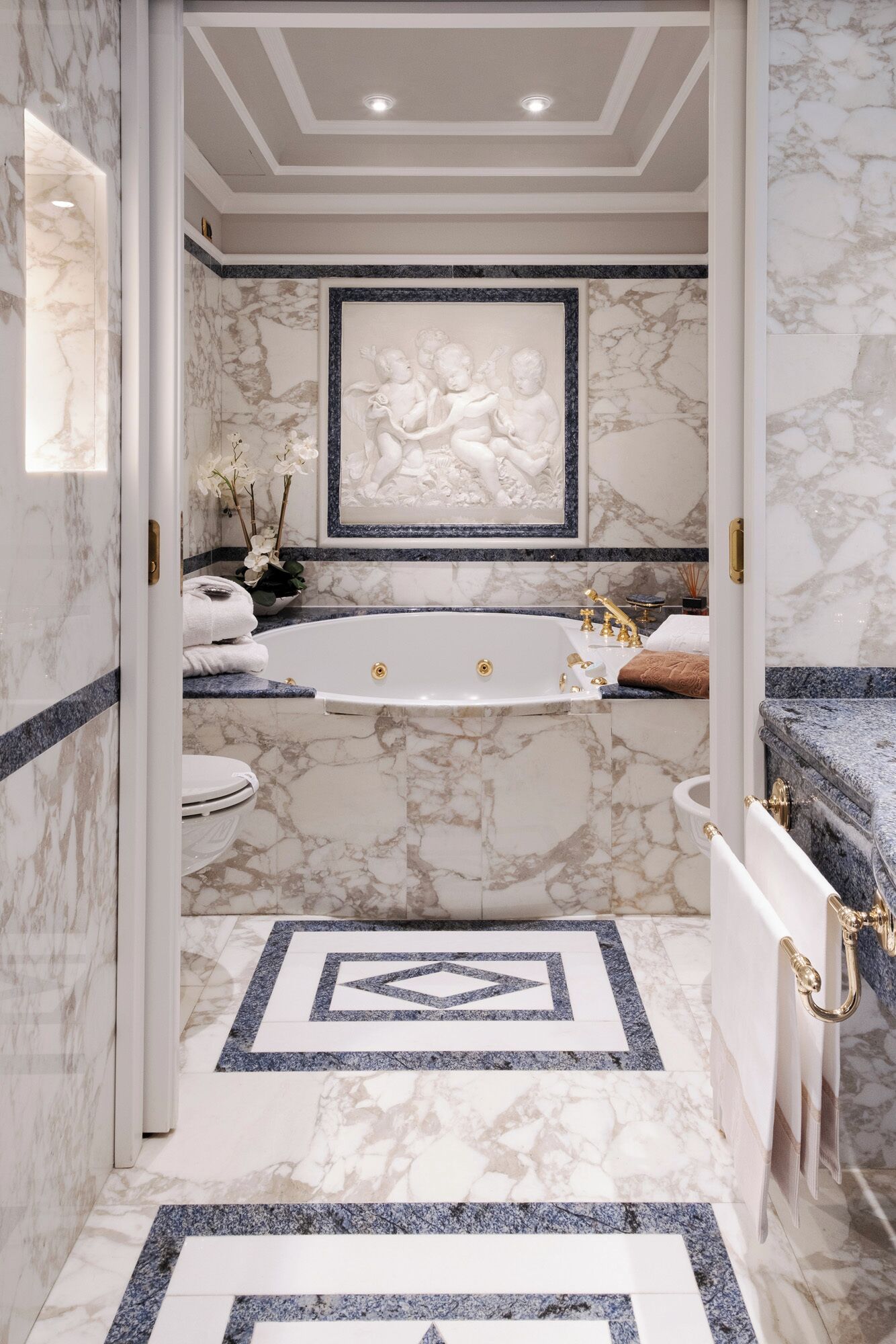 A luxurious bathroom with a marble floor, a large bathtub, and a framed artwork above the sink.