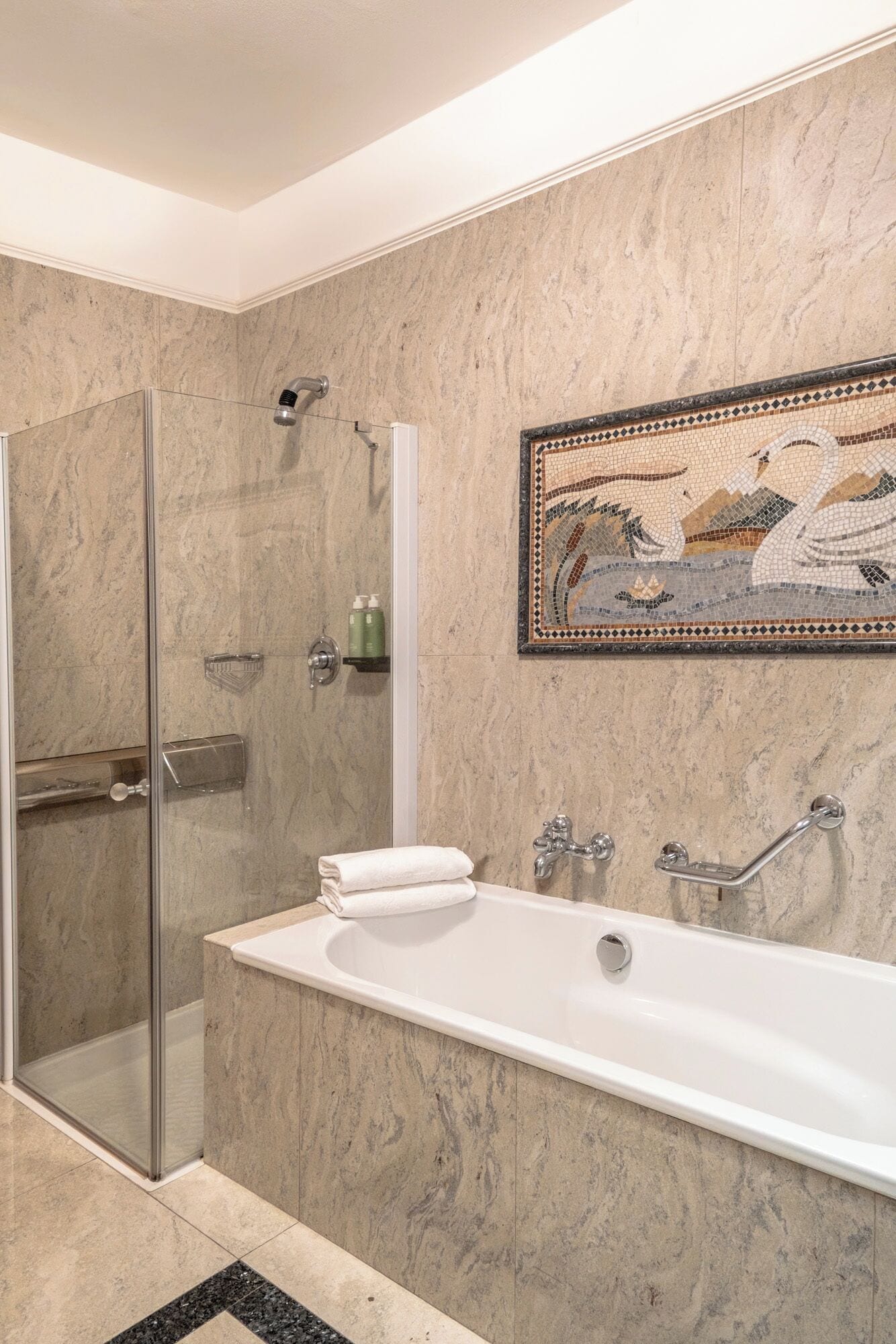 A modern bathroom with a glass-enclosed shower, a freestanding bathtub, and a mosaic artwork on the wall.