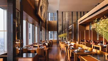 A spacious restaurant with high ceilings, large windows, and a variety of seating arrangements.