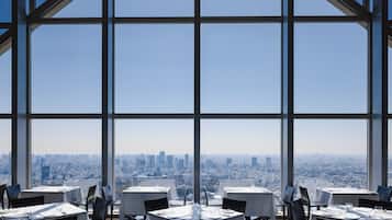 A restaurant with tables set for dining, large windows offering a city view.