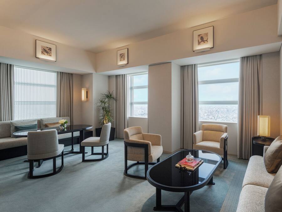 Habitación de hotel con sofá, sillas, mesa de centro, mesa de comedor y vista a la ciudad.