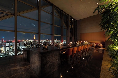 A high-rise bar with a panoramic city view, large windows, and modern furnishings.