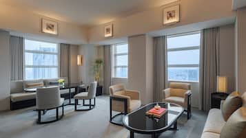 A modern hotel room with a sofa, armchairs, a coffee table, and a dining area.