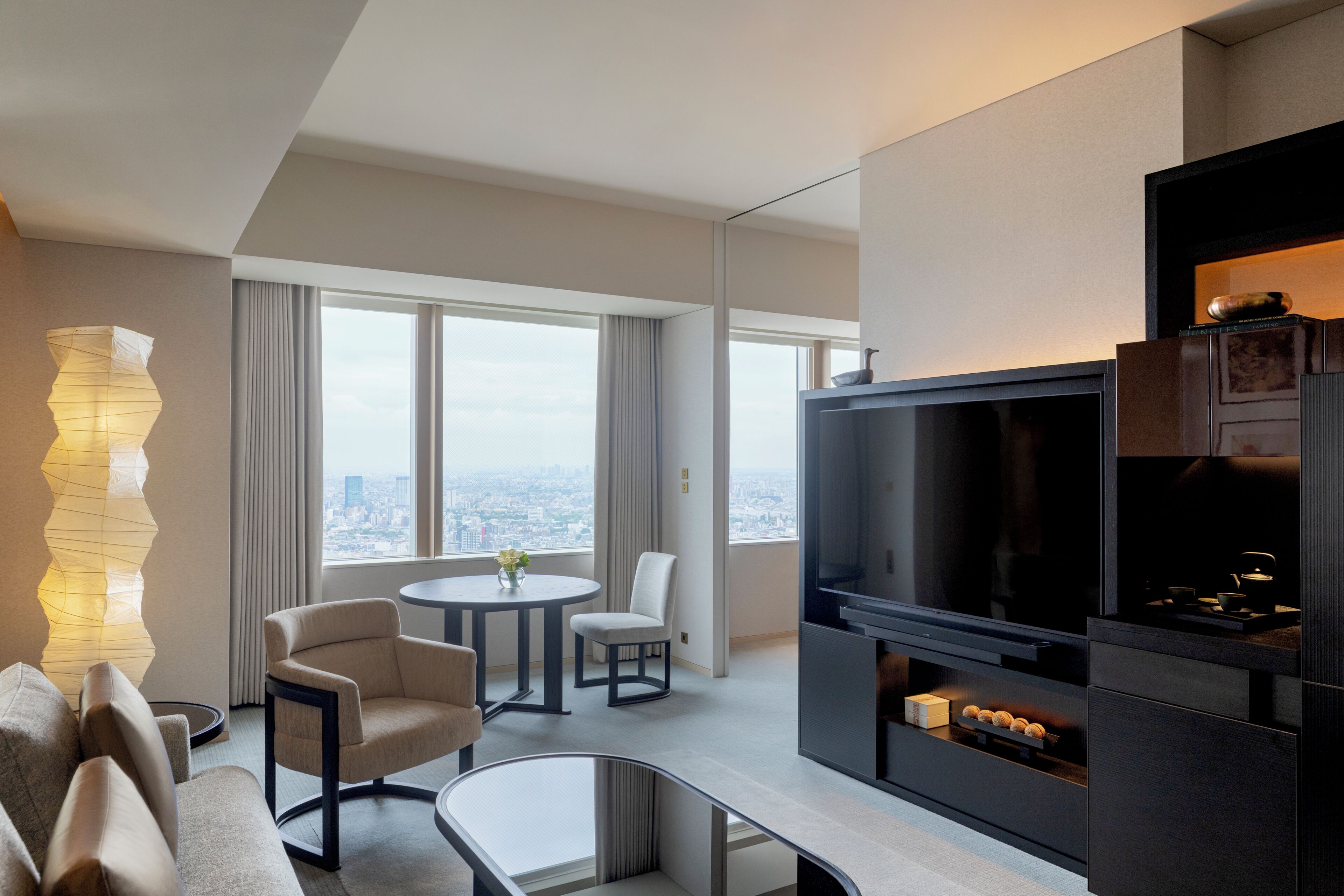 Una sala moderna con televisor de pantalla plana, una zona de comedor con mesa redonda y un amplio ventanal con vistas a la ciudad.