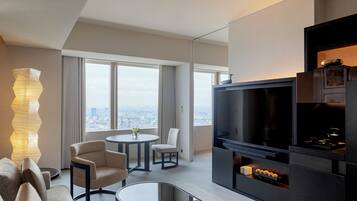 Una sala moderna con televisor de pantalla plana, una zona de comedor con mesa redonda y un amplio ventanal con vistas a la ciudad.