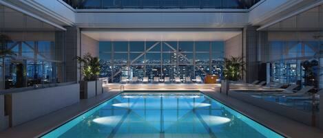 A modern indoor swimming pool with a cityscape view, large windows, and lounge chairs.