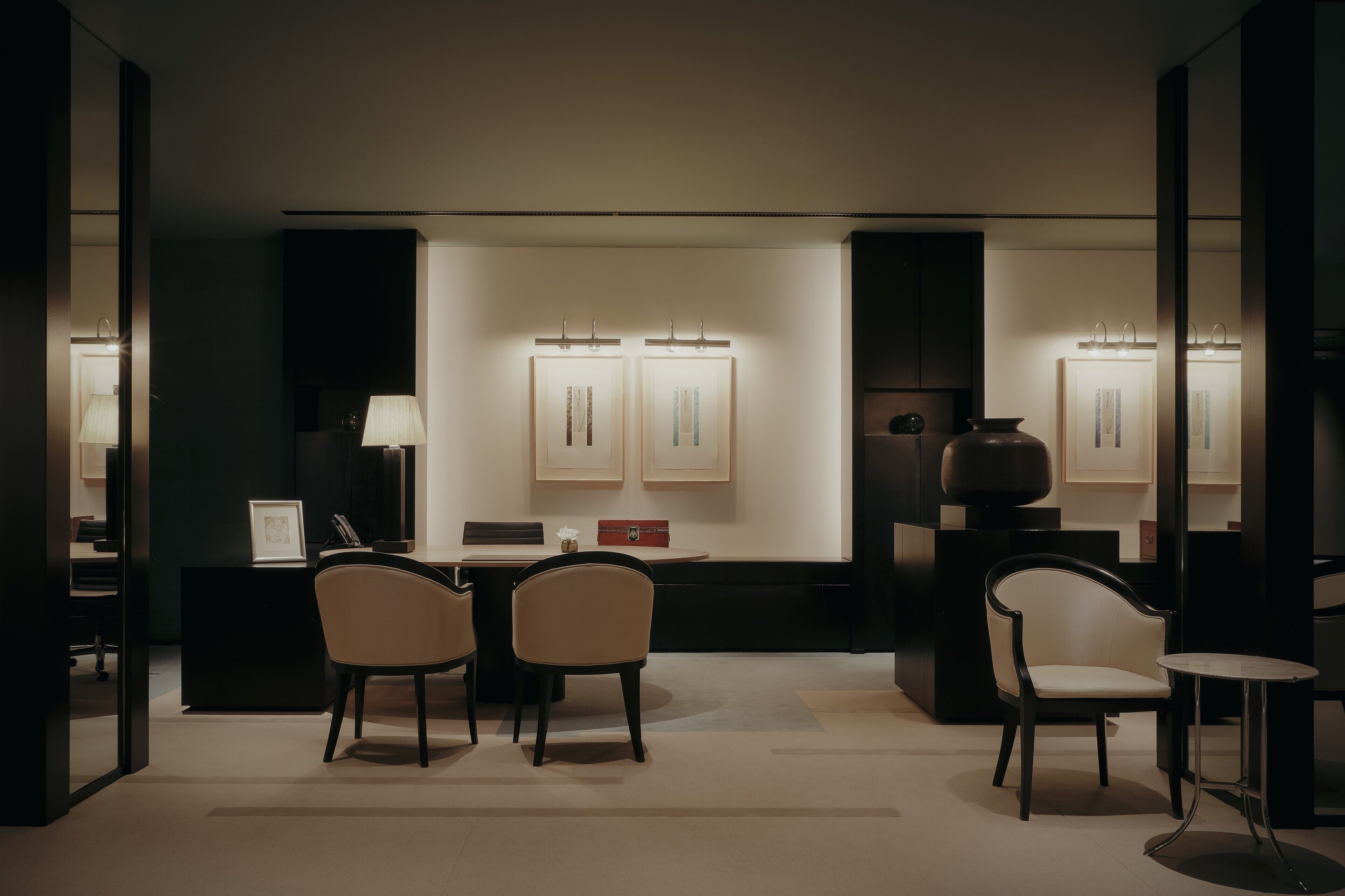 Un intérieur moderne avec un comptoir d’accueil aux tons sombres, deux œuvres d’art encadrées accrochées au mur et une petite table avec une chaise.