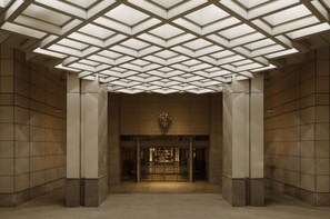 A modern building entrance with a geometric ceiling design, large glass doors, and a central emblem. - Park Hyatt Tokyo (Tokyo)