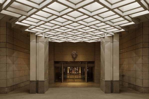 A modern building entrance with a geometric ceiling design, large glass doors, and a central emblem.