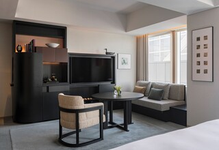 A modern hotel room with a flat-screen TV, a sofa, a chair, and a small table.
