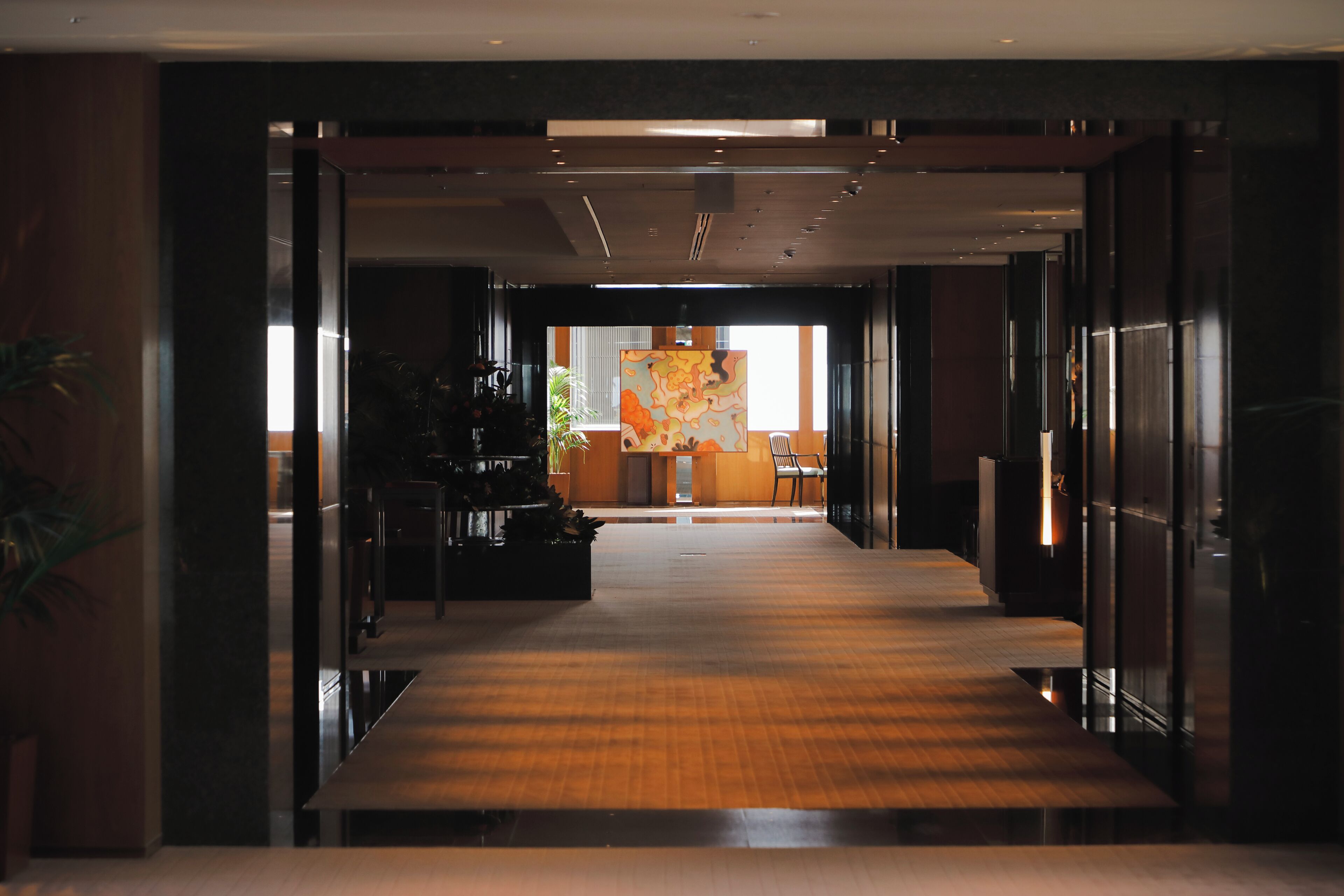 A corridor with a wooden floor leading to a room with a large abstract painting.