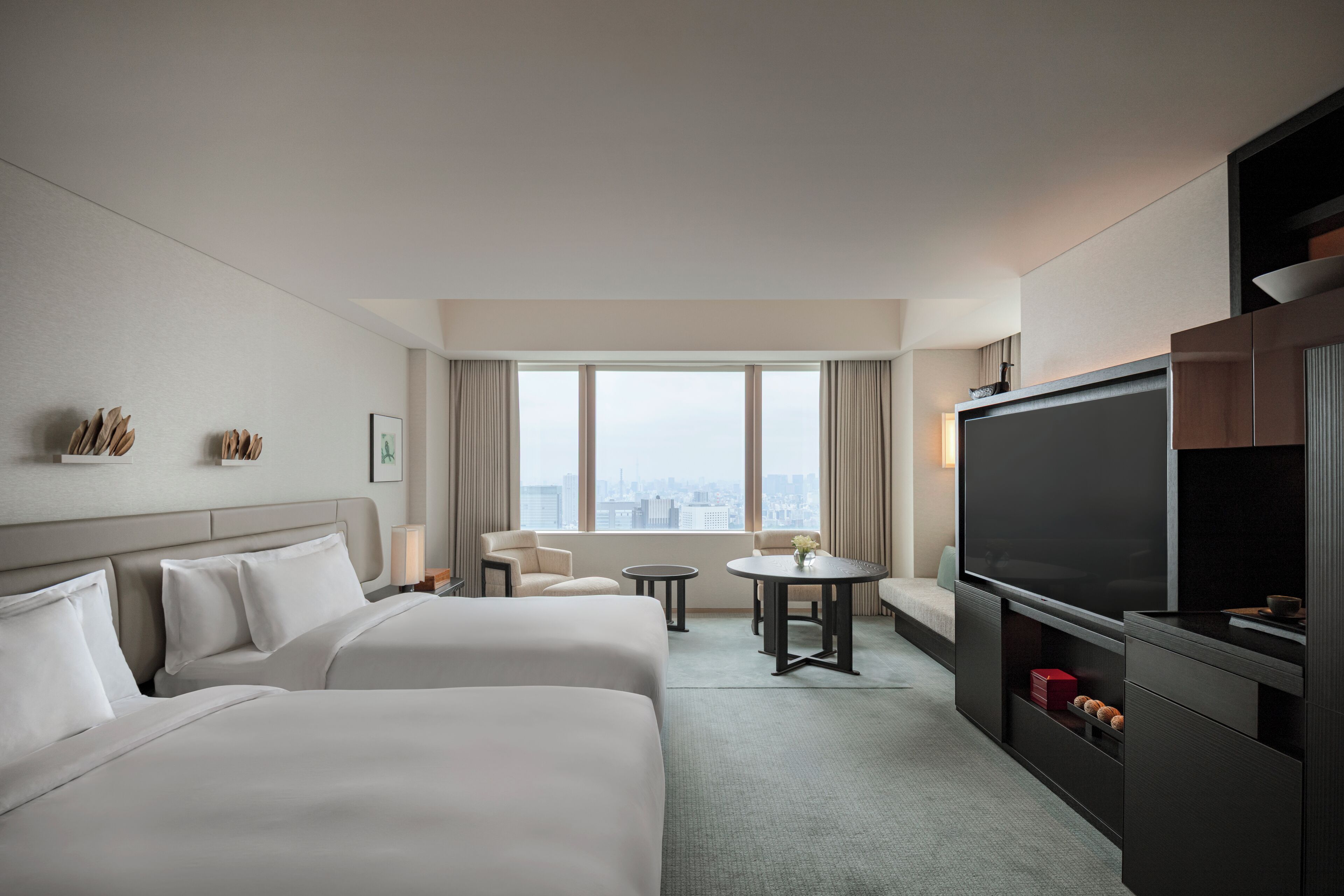 Ein Hotelzimmer mit zwei Betten, einem Fernseher, einem kleinen Tisch und Blick auf die Stadt.