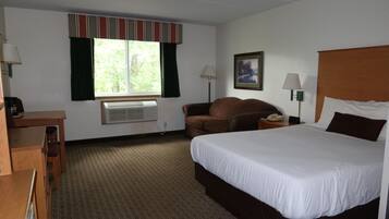 A hotel room with a large bed, a desk, a chair, a window with curtains, a wall-mounted lamp, and a framed picture.