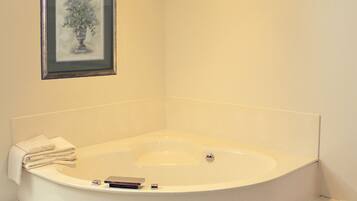A corner bathroom with a freestanding bathtub, a framed picture on the wall, and a towel on the tub's edge.