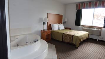A hotel room with a large bathtub, a bed with a headboard, two bedside lamps, and a window with curtains.