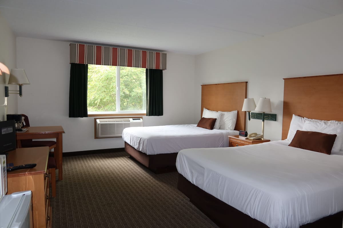 Habitación de hotel con dos camas, un escritorio, una silla, una ventana con cortinas y una lámpara.