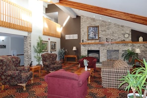 A spacious living room with a fireplace, patterned carpet, and multiple seating options including a red sofa and patterned armchairs.